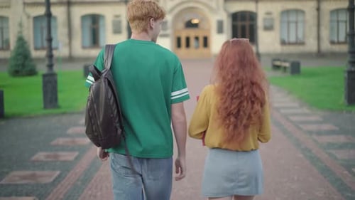 Back View of Young Redhead Caucasian Man and Woman Walking on Campus and Talking. Middle Shot of