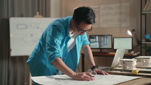 Asian Man Engineer With A Laptop Looking At Blueprint While Working At The Office
