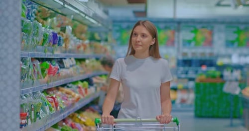 Beautiful Girl Walks Through the Supermarket with a Grocery Cart Shopping for Groceries
