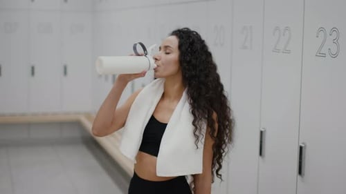 Woman Drinks Water in Locker Room After Workout