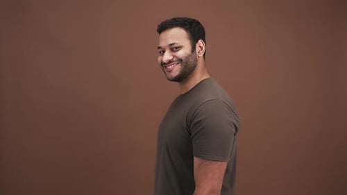 Playful Indian Man Flirting Pointing to Camera with Both Hands and Winking Brown Studio Background