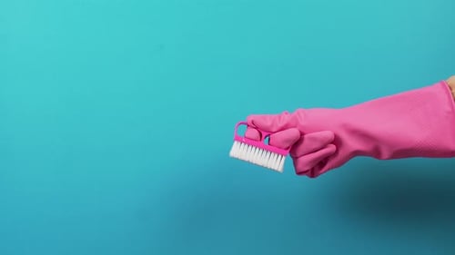 Rechts eine Hand mit rosa Handschuhen und einer Hartflor-Reinigungsbürste aus Kunststoff