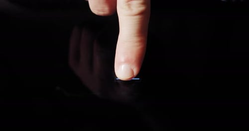 Finger presses glowing blue button on futuristic surface