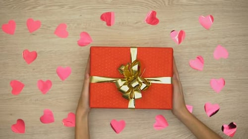 Lady Putting Present on Table Covered With Heart-Shaped Confetti, Top View