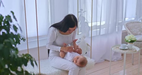 Woman Holds Baby on Swing Indoors