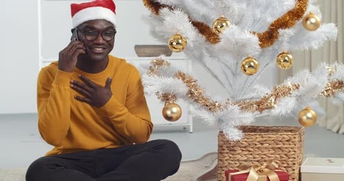 Young Man Chatting on Phone Next to Christmas Tree