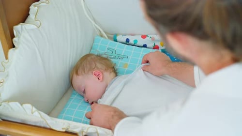 Man Covers Sleeping Infant with Blanket in Crib