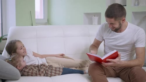 Father Reading to Daughters on White Couch