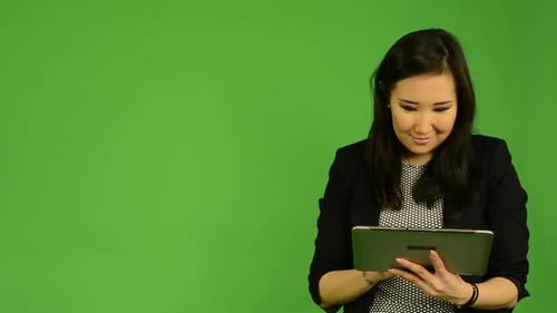 Young Attractive Asian Woman Works on Tablet and Smiles - Green Screen Studio