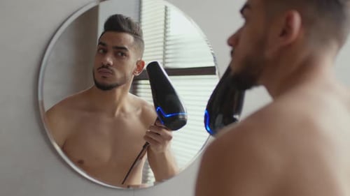 Man Prepares Hair with Blow Dryer in Bathroom Mirror