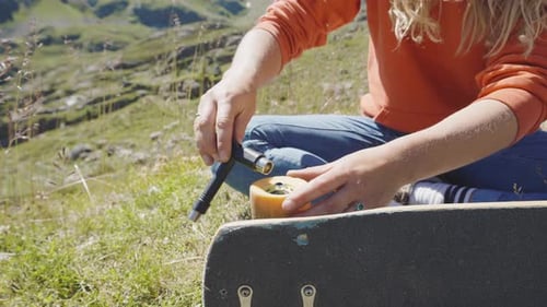 Woman Repairs Skateboard Wheel in Mountain Setting