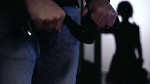 Man Buckling Belt Threatening Silhouette in Dark Room