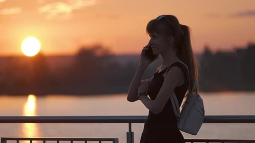 Happy Young Woman Relaxing on Summer Park Lakeside Talking on Her Mobile Phone Outdoors on Warm