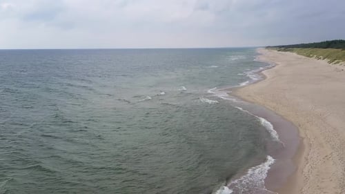 AERIAL: Flying Backwards and Revealing Sandy Beach on a Cloudy Day wih Sea and Green Hill