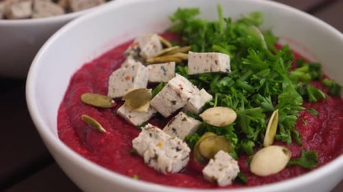 Close Up of Creamy Beet Soup with Tofu and Parsley Leaves Being Decorated with Pumpkin Seeds.