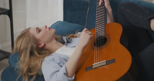 Woman Plays Guitar Lying on Blue Couch