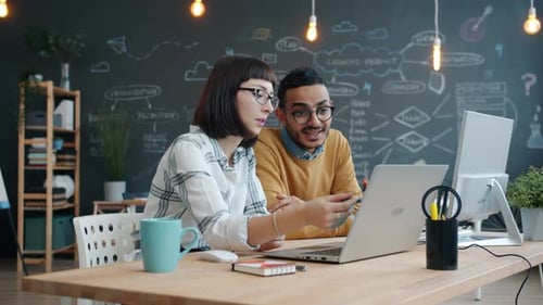 Colegas felizes conversando, fazendo “high-five” e rindo na mesa no local de trabalho