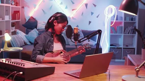 Asian Female Singer Playing Guitar and Singing in Home Recording Studio