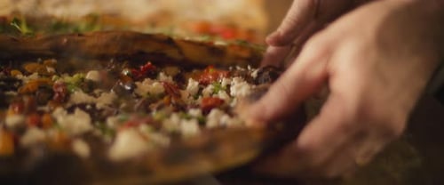 Delicious al taglio pizzas with different toppings being placed on a wooden surface in a pizza cafe.