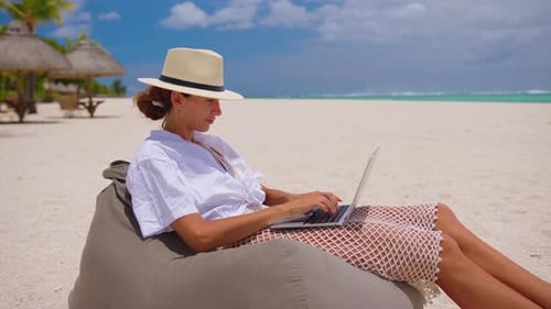 Erfolgreiche Geschäftsfrau mit gelbem Hut arbeitet am Laptop am Meer
