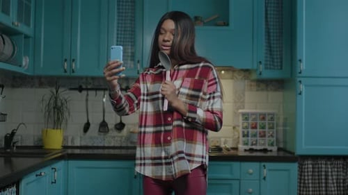 Woman Sings into Spoon in Kitchen Holding Phone