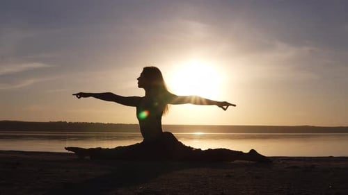 Hermosa silueta de mujer haciendo yoga split en la costa del mar