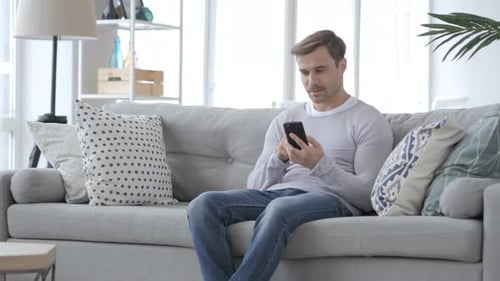 Man Using Smartphone on Couch in Sunny Living Room