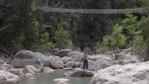 Une femme en pantalon large fait des exercices méditatifs sur le rocher au milieu du ruisseau