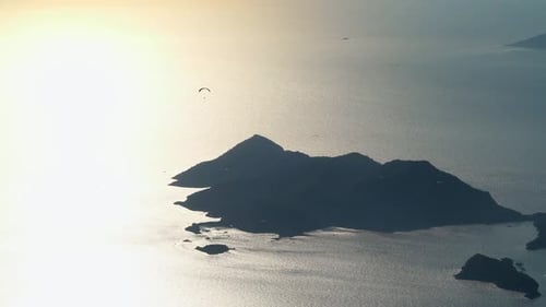 Gleitschirmflieger fliegen mit Gleitschirmfliegen im Himmel über Wald, Berggipfel und Meer