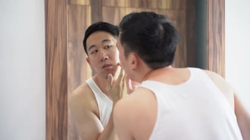 Puzzled Asian Man Checking Acne Problems While Looking in Mirror