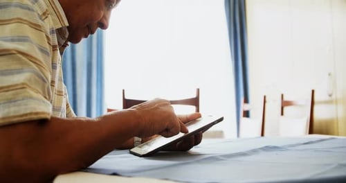 Senior Man Uses Tablet at Table Indoors