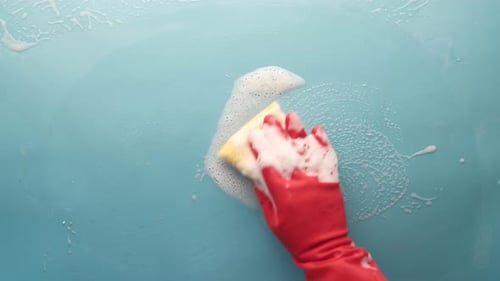 Gloved Hand Cleaning a Blue Surface with Sponge
