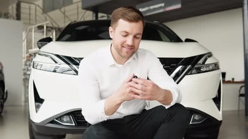 Portrait of a Young Man with Keys Near a New Car in a Car Dealership