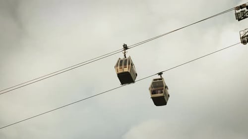 Cable car with modern cabin going up on grey cloudy background.