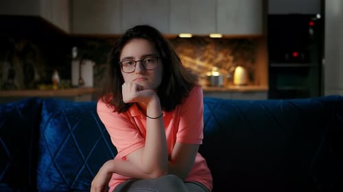 Young Woman Sitting on Blue Couch with Pensive Expression