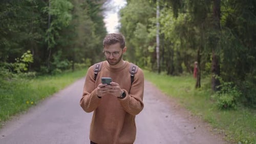 Smiling Man with Glasses with a Beard Walks Through the Woods with a Backpack and Prints a Message