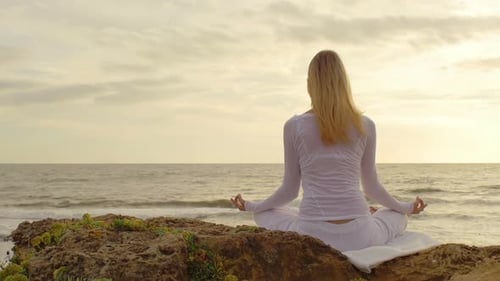 Jeune femme pratiquant le yoga sur la plage au coucher du soleil