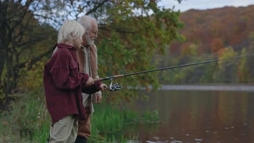 Boy Holding Fishing Rod While Standing with Grandpa on Lake