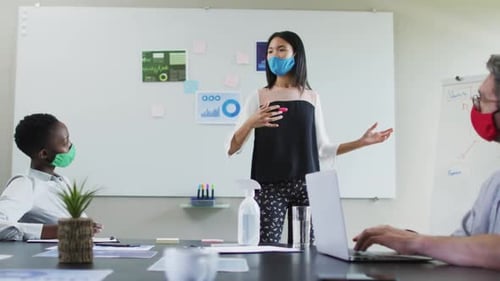 Asian woman wearing face mask giving presentation to her colleagues in meeting room at modern office