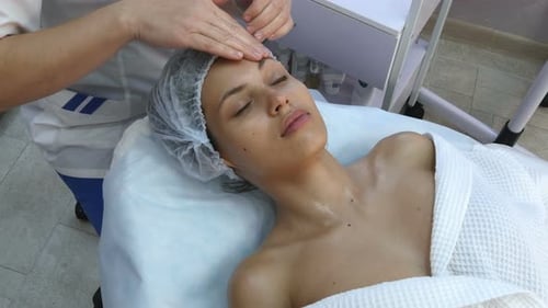Beautiful Young Woman Getting Facial Massage with Closed Eyes in a Spa Salon