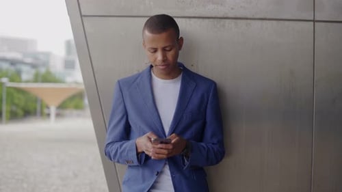 Smiling Man Using Phone Leaning on Urban Wall