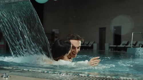 Divertida pareja a caballitos en la piscina del spa. Hombre y mujer guapos abrazando el jacuzzi