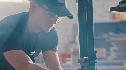 Man in a Carpentry Workshop Cutting Pieces of the Wooden Detail Using a Cutting Machine
