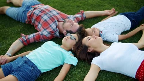 Family Lying on Green Grass in Circle. Cute Kids and Parents Relaxing in Field