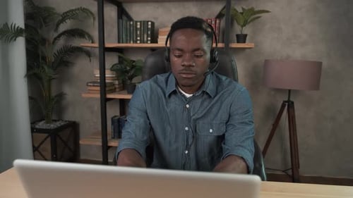African Man Employee Works in the Office at the Computer. Black Businessman with Wireless Headset