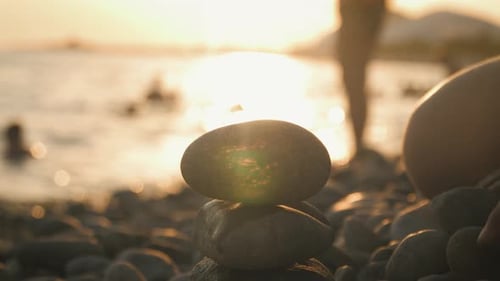 Mano con piedras de guijarros sobre un fondo de puesta de sol y mar. Concepto de equilibrio.
