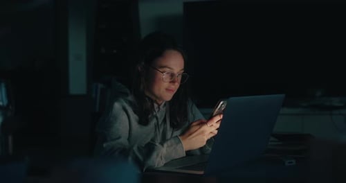 Woman using laptop and mobile phone at night