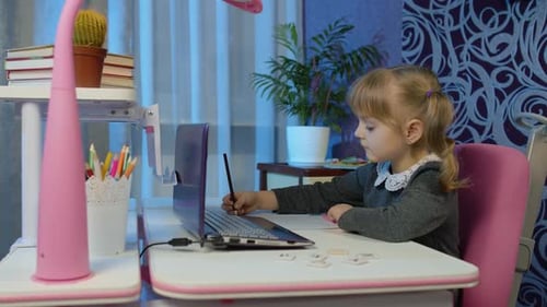 Child Writes in Notebook at Desk with Laptop
