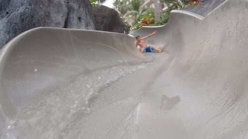 A boy plays on a waterslide water slide in a pool at a hotel resort.