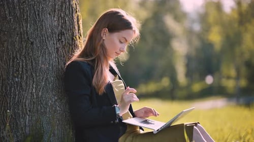 A Girl with a Laptop Resting in the Park By a Tree